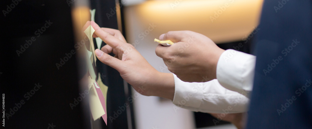 Obraz premium Hands of businesspeople and colleague brainstorm for planning and strategy of business and marketing at office, group of team meeting for creative with writing on post it sticker, business concept.