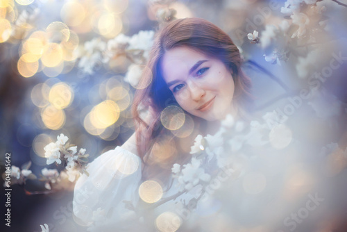 spring portrait of an adult happy woman in a blooming garden, sun rays and glare, april flowers girl