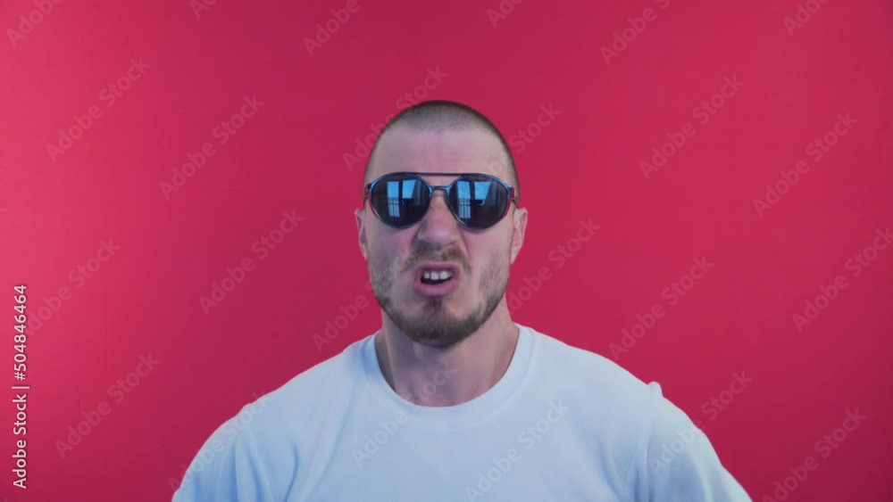 Angry Man Screams With Mouth Wide Open Into The Camera. Spreads Hands to the Parties, Grabs the Head. A Man in Sunglasses on a Red Background Shouts, Emotions of Evil. Threat of Violence Angry Man Screams With Mouth Wide Open Into The Camera. Spreads Hands to the Parties, Grabs the Head. A Man in Sunglasses on a Red Background Shouts, Emotions of Evil. Threat of Violence