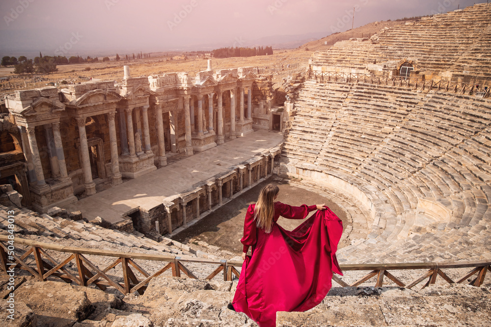 Adventure photo tourist woman in red dress on background Amphitheater in Hierapolis ancient city Pamukkale Turkey