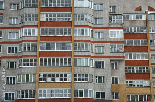 Многоэтажный жилой дом из серого кирпича с оранжевыми и красными лоджиями и балконами.