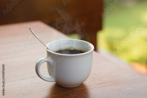 Cups of black coffee with smoke on wood table with natural background.