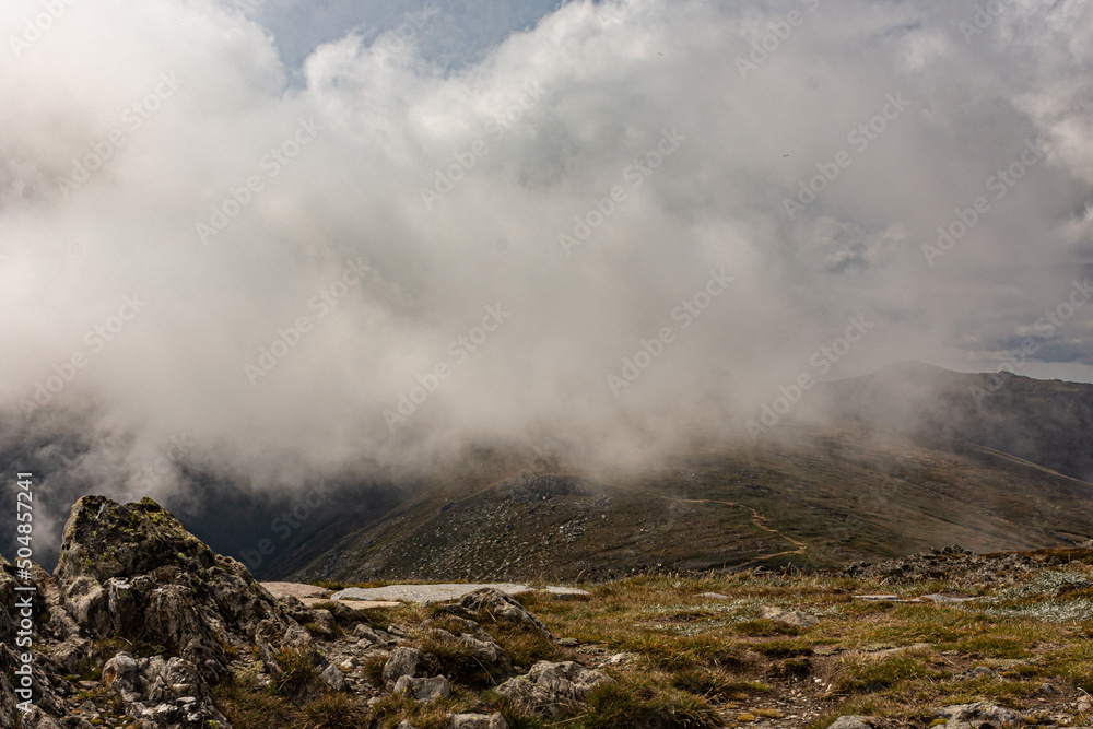 Fog hovering over alpine mountain ranges on winters day. Misty cloud covering mountain valley from summit Fog hovering over alpine mountain ranges on winters day. Misty cloud covering mountain valley from summit