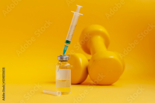 syringe is stuck in a jar, there are dumbbells on a yellow background next to it. the concept of doping in sports, steroids, testosterone and other drugs prohibited in sports.