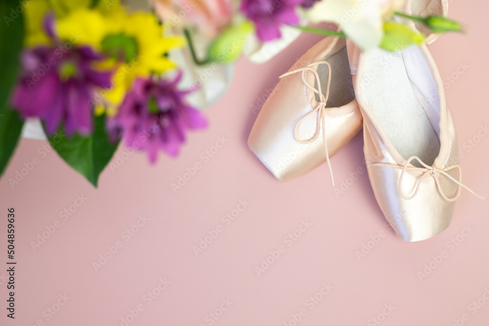 Ballet pointe shoes and a bouquet of flowers on a pink background. Top view, place for text.