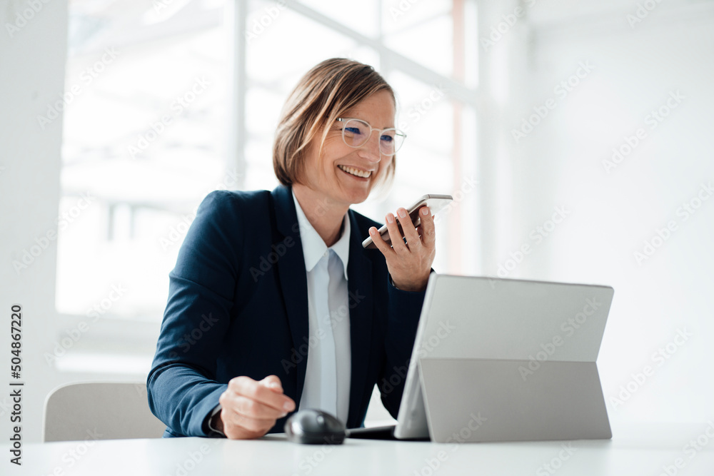 Happy businesswoman talking on mobile phone sitting at desk in office Happy businesswoman talking on mobile phone sitting at desk in office