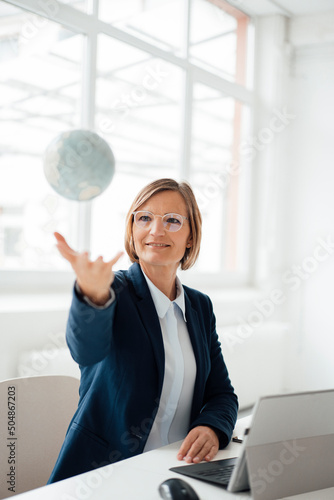 Businesswoman catching globe sitting at desk in office photo