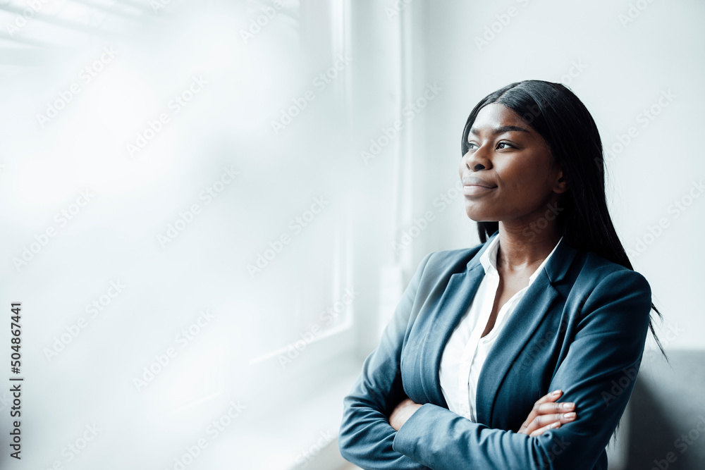 Young businesswoman looking through window standing with arms crossed in office Young businesswoman looking through window standing with arms crossed in office