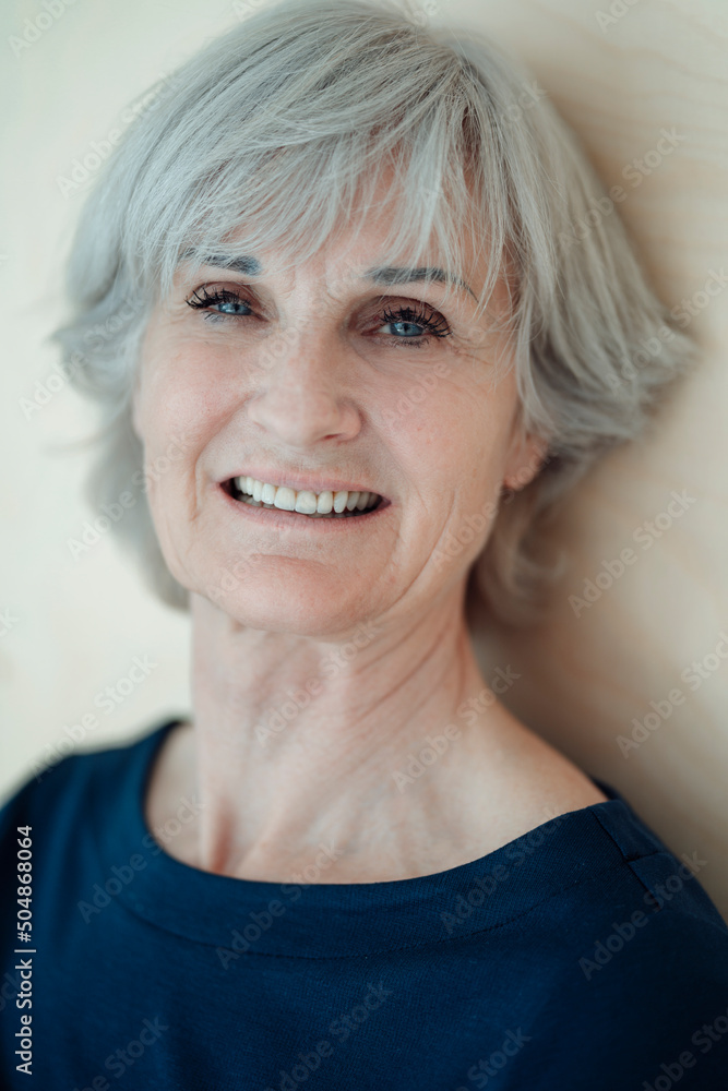 Smiling senior woman with gray hair in front of wall Smiling senior woman with gray hair in front of wall