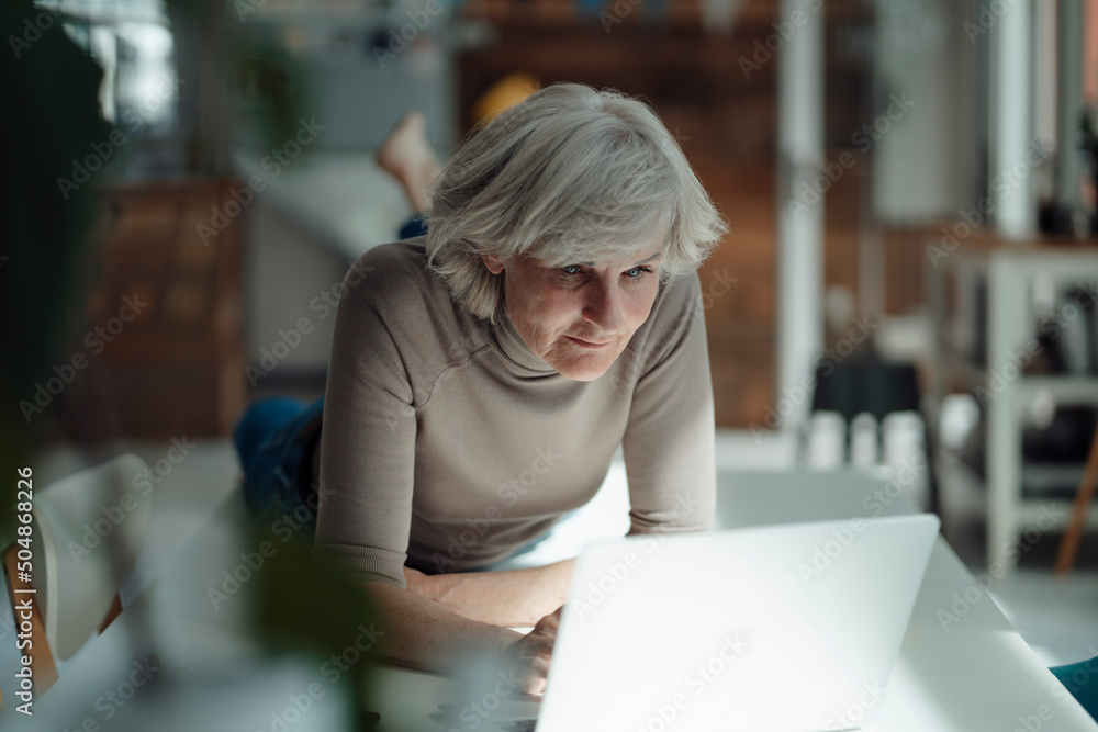 Senior woman using laptop lying on desk in office Senior woman using laptop lying on desk in office