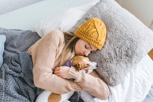 Woman wearing warm clothing cuddling with dog in bed