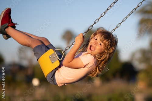 Emotional portrait of a child in the playground. Outdoor kids activity. Little boy having fun on a swing on the playground in public park on autumn day. Happy child enjoy swinging.