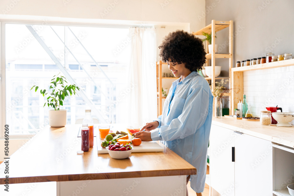 Happy woman cutting fruit on cutting board in kitchen at home Happy woman cutting fruit on cutting board in kitchen at home