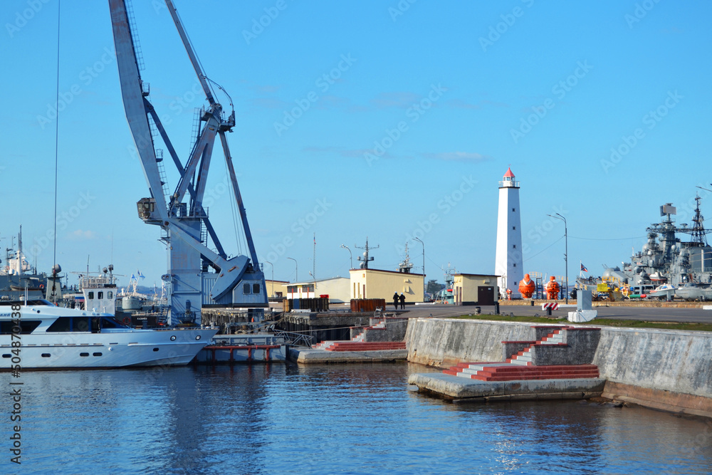 Baltic Sea embankment in Kronstadt with a view of ships and a wooden white lighthouse