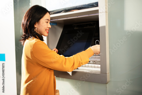 Happy smiling young woman withdrawing money from credit card. Young woman using ATM machine