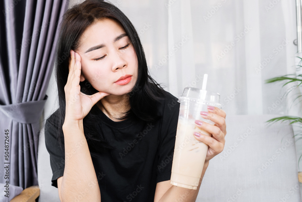 Asian woman having a headache and dizzy after drinking ice coffee, headache triggered by caffeine concept Asian woman having a headache and dizzy after drinking ice coffee, headache triggered by caffeine concept