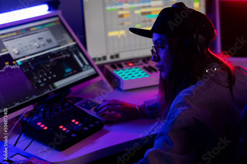 Beautiful caucasian girl in stylish clothes works in a recording studio with neon light in a cap and glasses. Close up