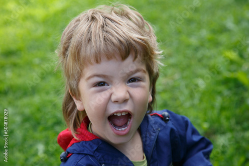 A little boy screams emotionally against the background of green grass.