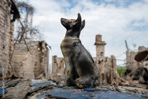 A clay figurine of a dog against the background of a destroyed house, burned down and broken as a result of a Russian army shell hitting it in the city of Irpen, UkraineA clay figurine of a dog agains photo