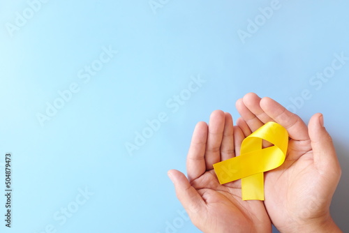 Top view of male hand holding yellow ribbon in blue background with copy space. Sarcoma or bone cancer and suicide prevention awareness concept.