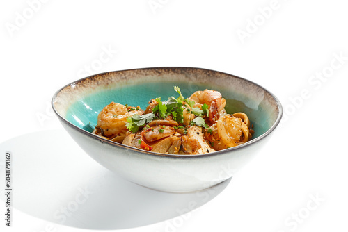 Pan asian food - udon with prawn, chicken wok on white background. Noodle with chicken and prawn in ceramic bowl. Indonesian wok with udon noodles. Spicy thai dish from noodle with shrimp and chicken.