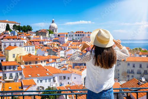A tourist woman looks at the beautiful cityscape of Lisbon, with the colorful houses and roofs at the Alfama district, Portugal