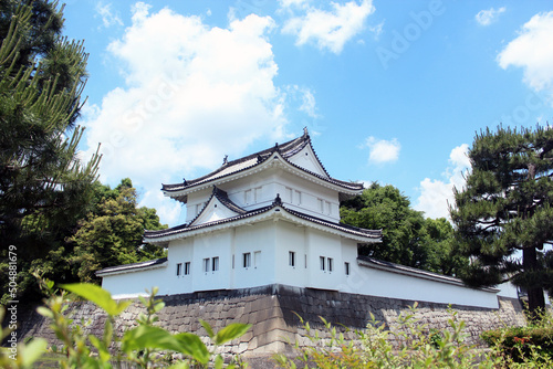Sunlight and blue sky and white clouds, white Japanese buildings on the city wall, surrounded by trees and green leaves