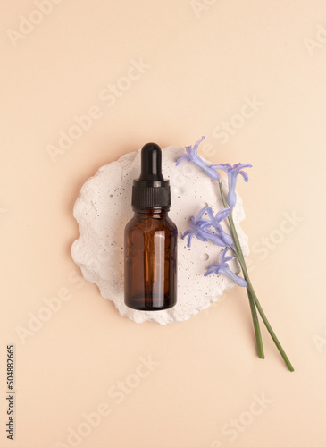Serum glass bottle with pipette and beautiful flower on beige background. Natural Organic Spa Cosmetic concept. Top view.