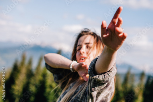 a young, slender girl with loose hair in a plaid shirt and jeans poses for sunny weather in the mountains