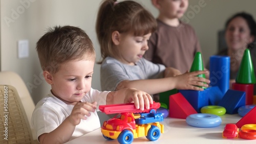 little boy and baby girl play in kindergarten. a group of children play toys cubes and cars on the table in kindergarten. happy family preschool education concept. nursery indoor baby toddler home