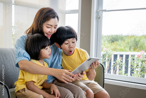 mother with two sons They are playing tablets together on the sofa in the house together happily and happily.