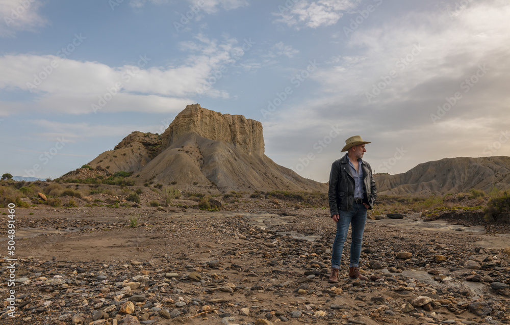 Adult man in cowboy hat in desert against rock and sky