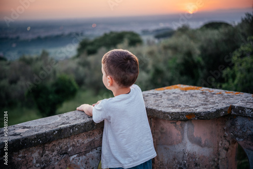 Back view of a littlle boy looking at beautiful sunset over olive grove in hilly landscape of Italy photo