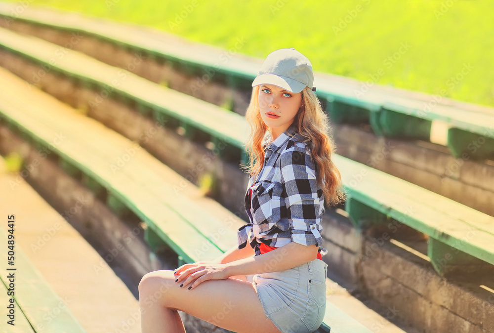 Portrait of beautiful young blonde woman wearing baseball cap, shorts and shirt in summer park Portrait of beautiful young blonde woman wearing baseball cap, shorts and shirt in summer park