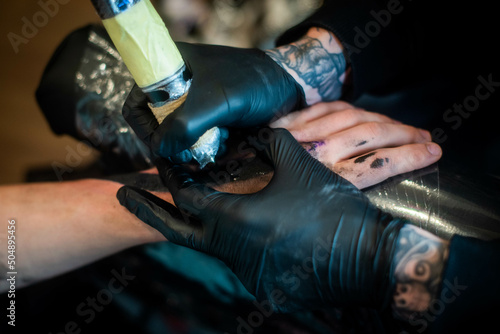 cropped shot of tattooing process on hand in salon. A professional tattoo artist introduces ink into the skin using a needle from a tattoo machine.Professional tattooist working in studio.