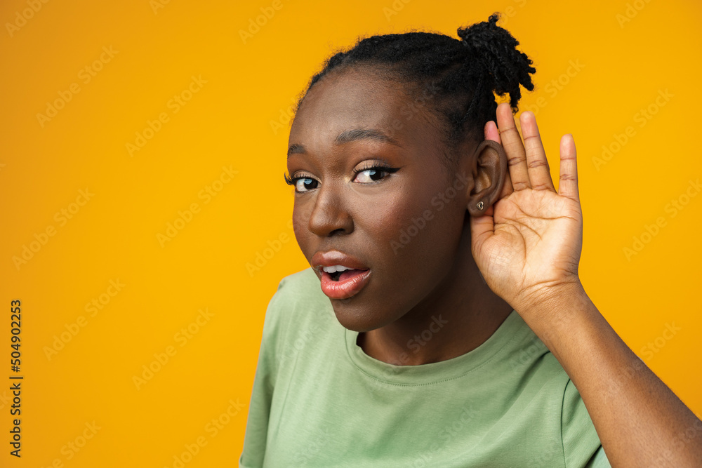 Dark-skinned woman on a yellow background overhears a conversation Dark-skinned woman on a yellow background overhears a conversation