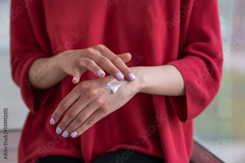 girl sits on the windowsill and applies cream on her hands © dinastiya