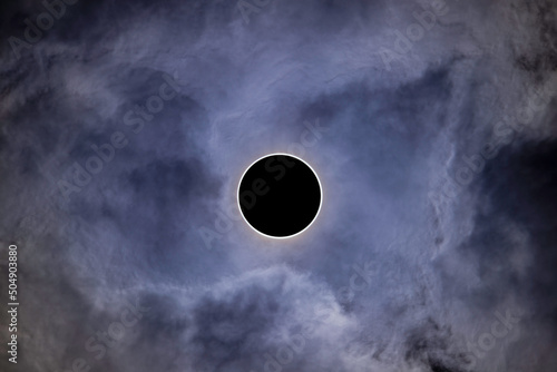 Zachmurzone niebo. W centrum kadru tarcza słoneczna przysłonięta czarną tarczą księżyca. Całkowite zaćmienie słońca.