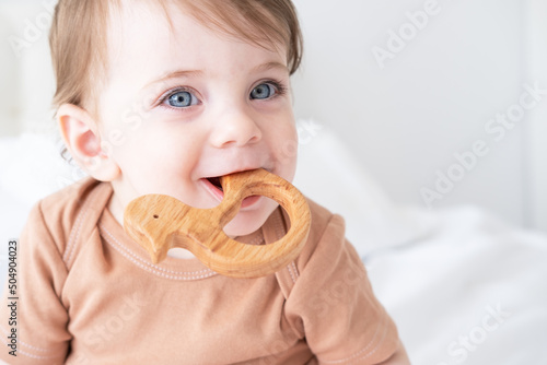Canvas Print portrait of baby girl with blue eyes plays with wooden toy teether for teeth on