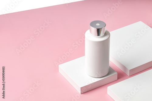 White plastic Bottle of cream with a dispenser on square podium and pink background. Mock up