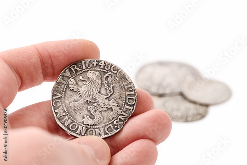 Obraz na płótnie Male hand holding old silver thaler with lion on reverse. Old coins on white background. Lion Daalder. Selective focus. w salonie