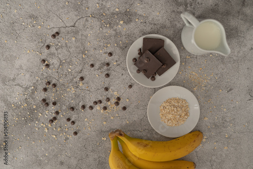 ingredientes para batido de avena, plátano y chocolate sobre fondo de piedra