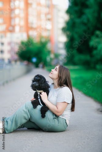 Plus size girl with long brown hair with dog on sidewalk, young woman and black poodle pet © natalialeb