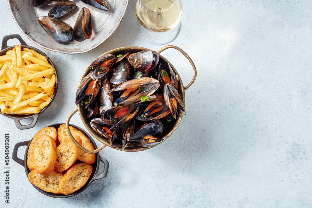 Cooked mussels with toasted bread, French fries, and white wine, overhead flat lay shot on a slate background with a place for text Cooked mussels with toasted bread, French fries, and white wine, overhead flat lay shot on a slate background with a place for text