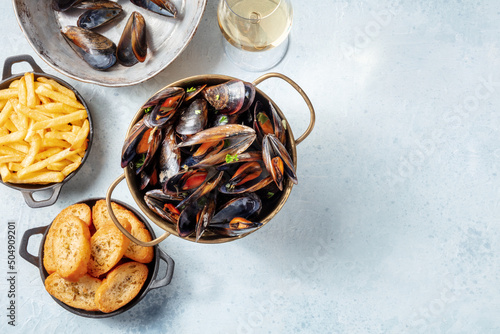 Cooked mussels with toasted bread, French fries, and white wine, overhead flat lay shot on a slate background with a place for text