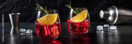Campari cocktails with fresh oranges, rosemary, a jigger and a shaker, a panorama on a black slate background photo