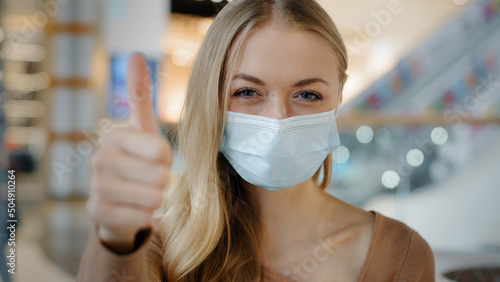 Indoors portrait caucasian woman patient girl female lady in face protective medical mask protecting health from coronavirus infection covid shows like puts thumbs up recommends wearing respirator