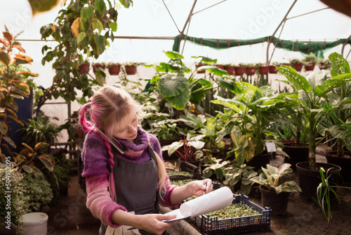 Young woman with pink hair holding tablet for writing and using smart phone for calling to clients in greenhouse of garden mall