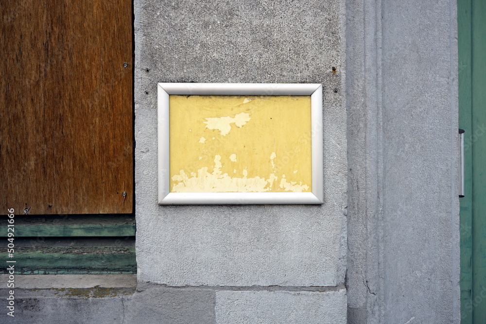 Obraz premium Verwahrlostes heruntergekommenes Schild mit gelbem Hintergrund und silbernem Rahmen auf grauem Beton in den Gassen der Altstadt von Brügge in Westflandern in Belgien