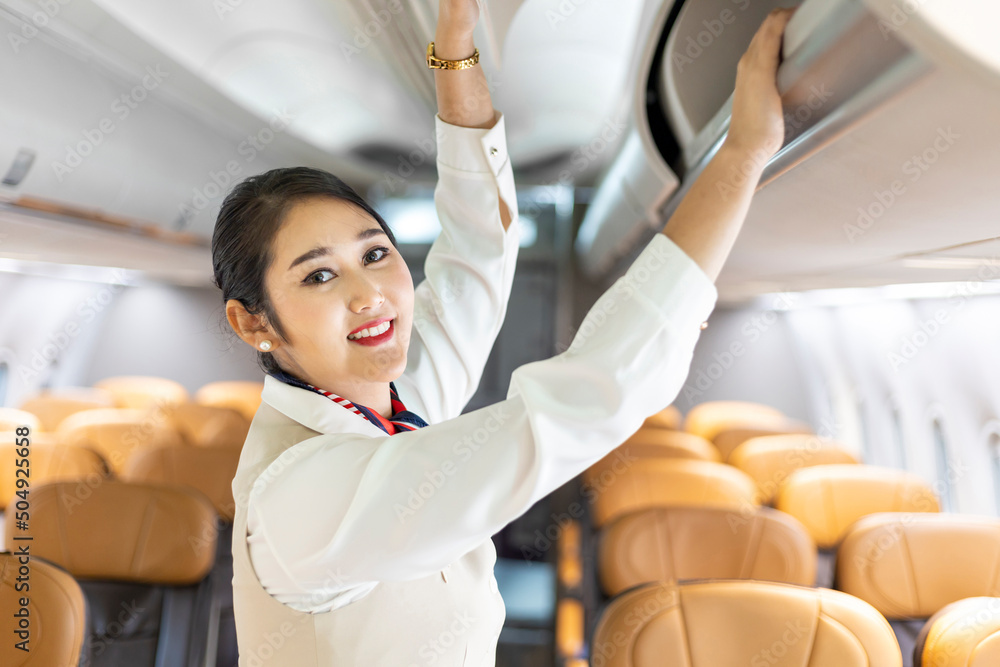 Asian female flight attendant closing the overhead luggage compartment